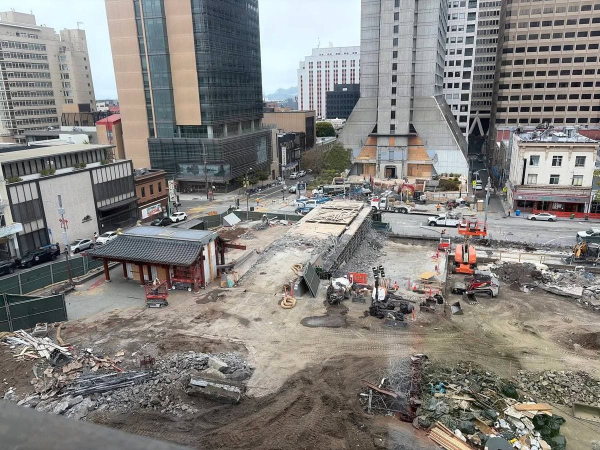 A cleared construction site with diggers and towers behind, the footbridge supports being removed