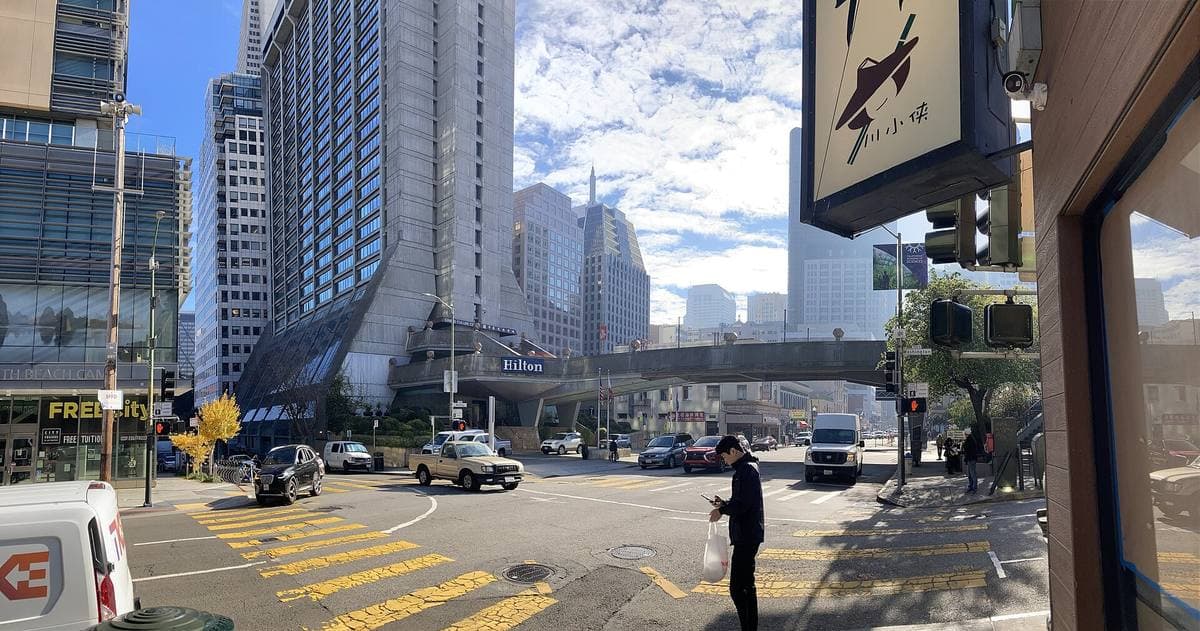 A concrete hotel tower beside Kearny Street, a footbridge crossing the road