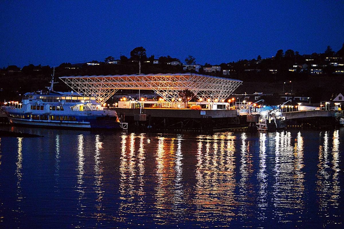 The lit canopy of a ferry terminal reflected in dark water