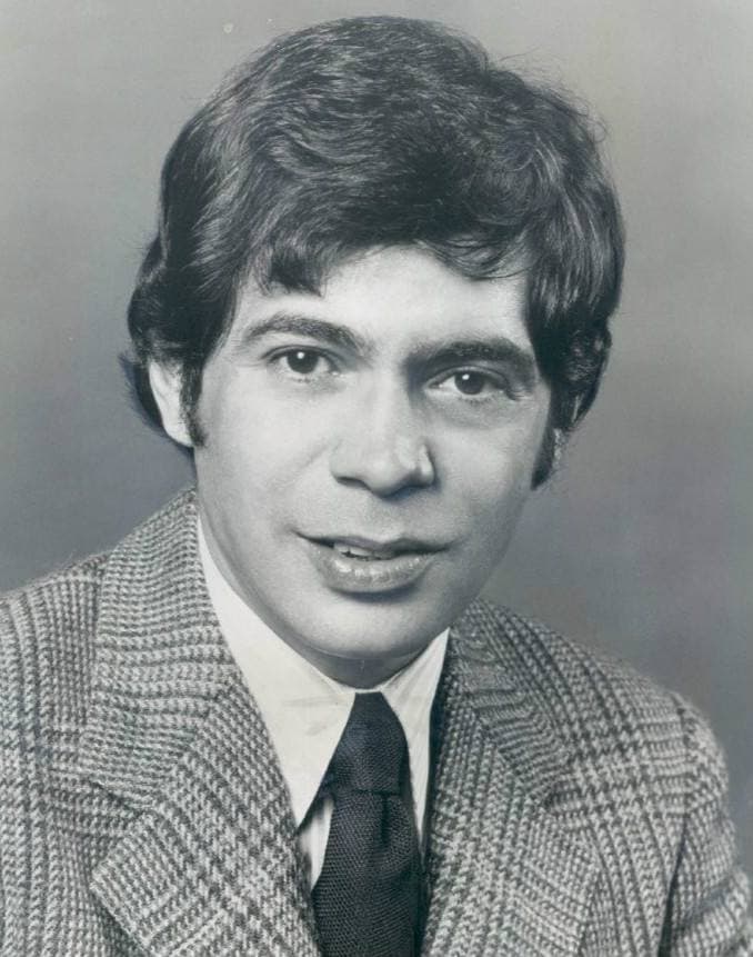 Head and shoulders portrait of Reni Santoni in a checked jacket and tie, smiling