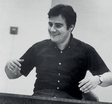 Lalo Schifrin laughing at a piano, one hand raised