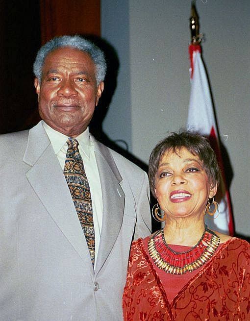 Ossie Davis in a grey suit beside Ruby Dee in a red dress and a beaded necklace