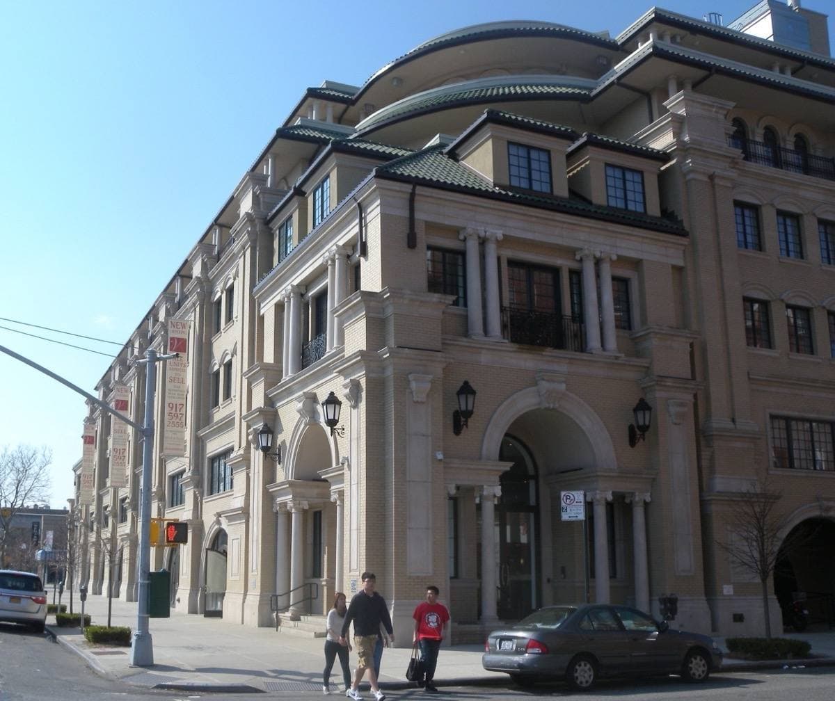 A tall cream condominium building on a street corner under a blue sky