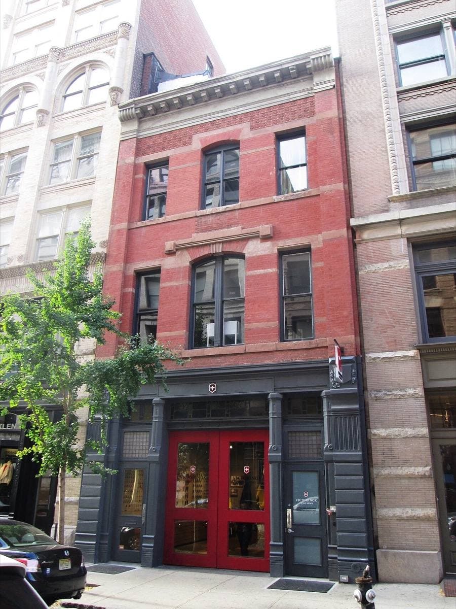 A narrow red-brick former firehouse with red doors between taller buildings