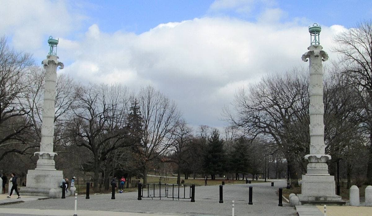 Two tall white columns topped with bronze bowls at a park entrance in winter