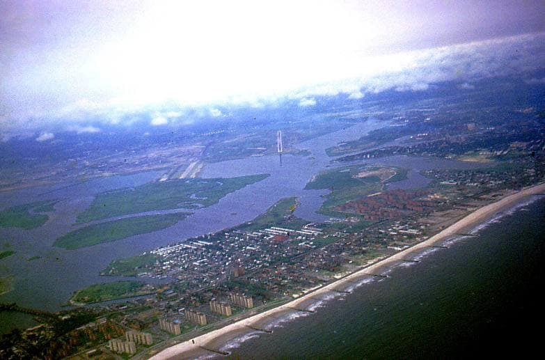 An aerial view of a long beach and the bay below an aircraft wing, hazy blue light