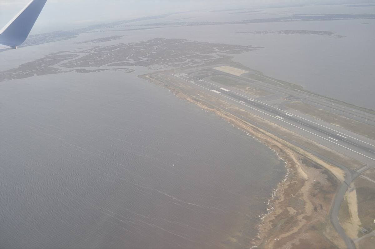 A runway seen from the air reaching out into grey water