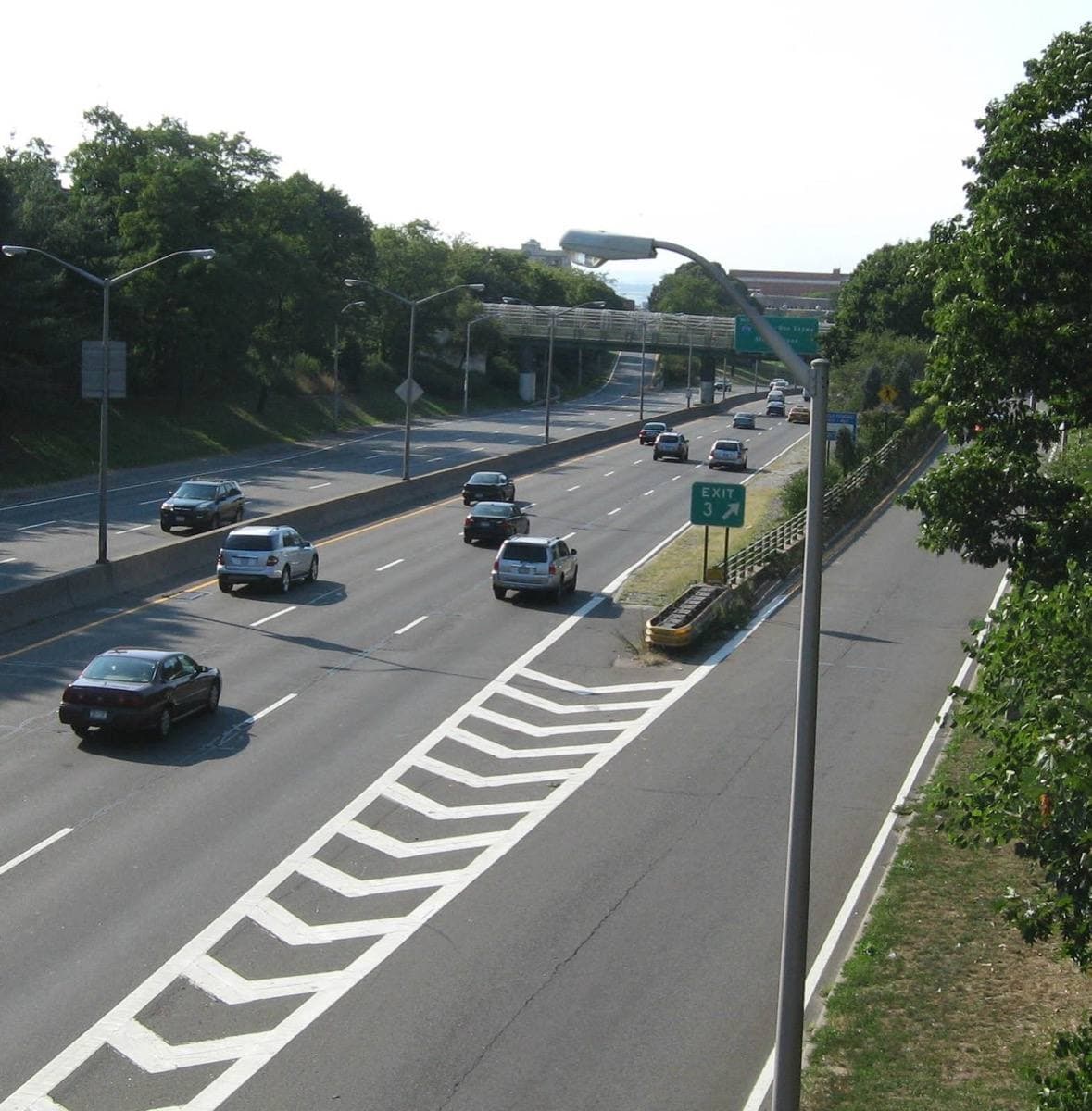 A sunken expressway with traffic, seen from a bridge, trees on both banks