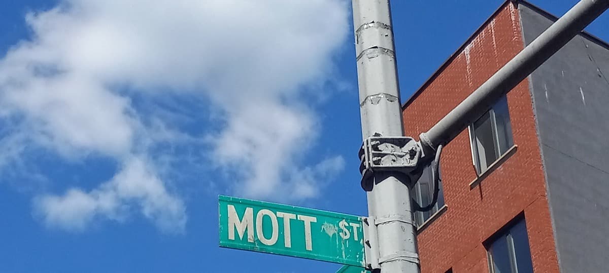 A green Mott Street sign above a Little Italy street