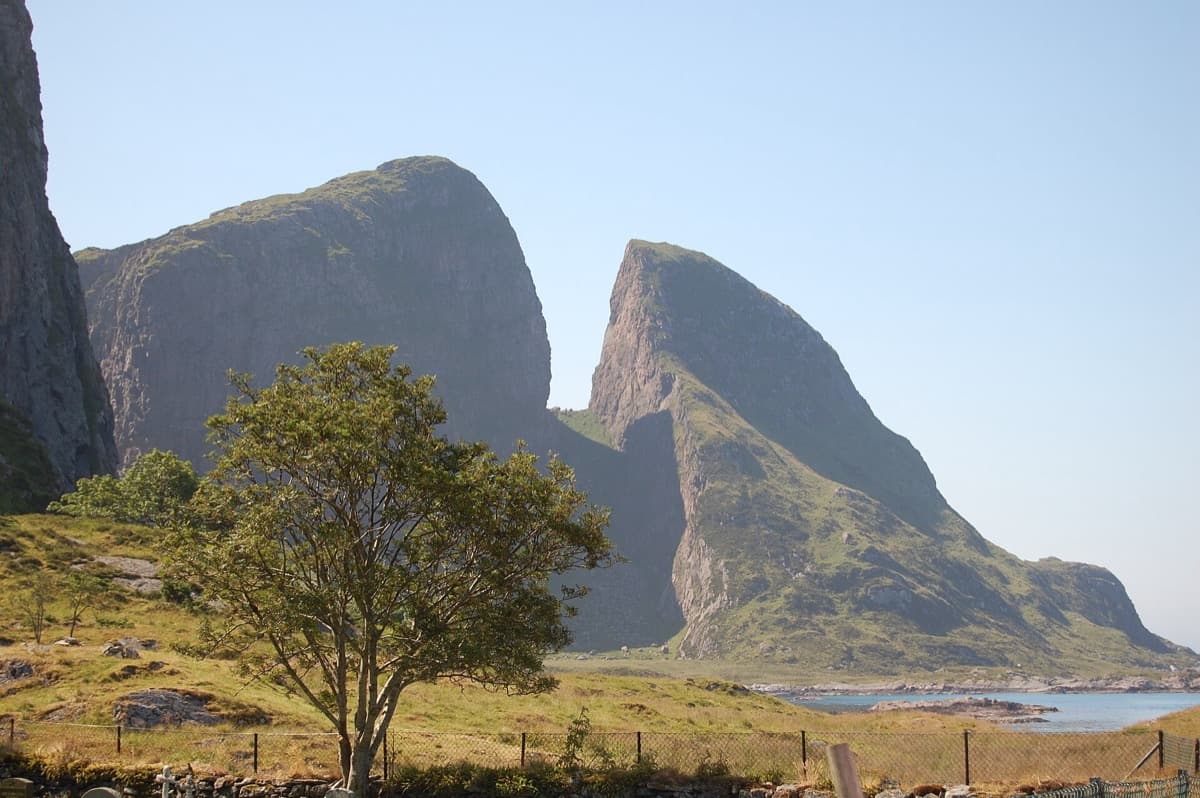 A steep grey mountain cleft in two, rising from a low green island beside the sea