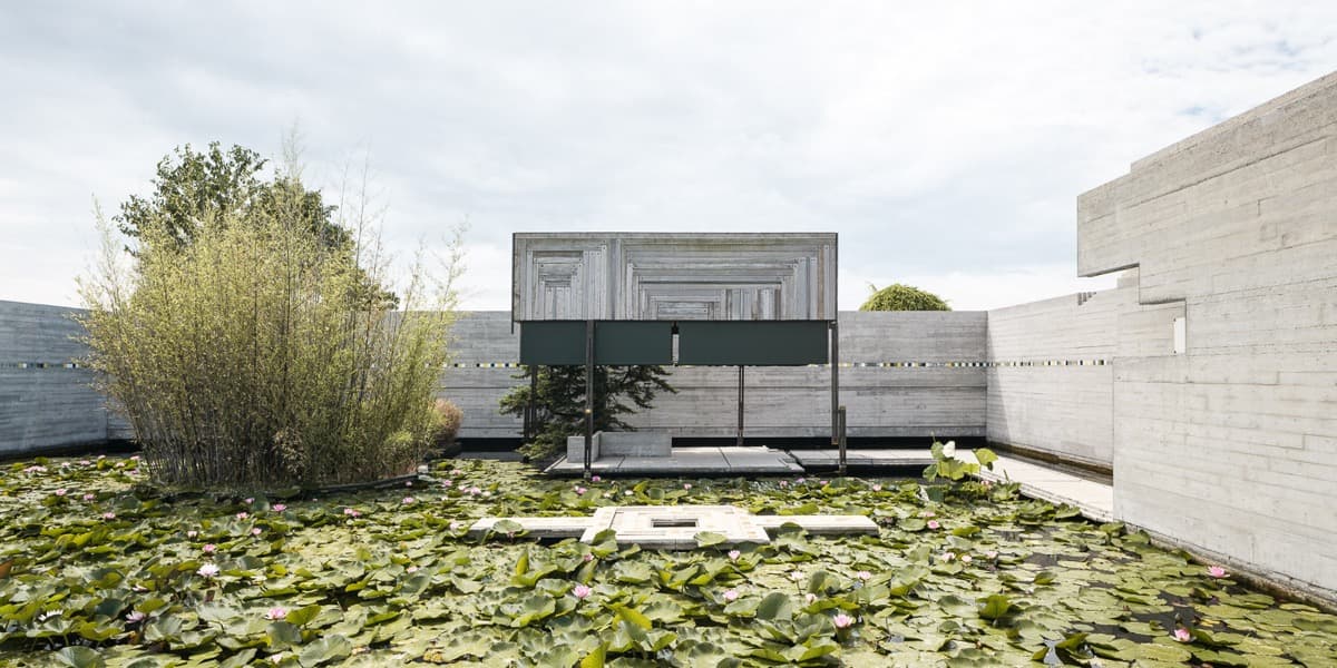 Low concrete walls and water channels in a green cemetery garden under an overcast sky