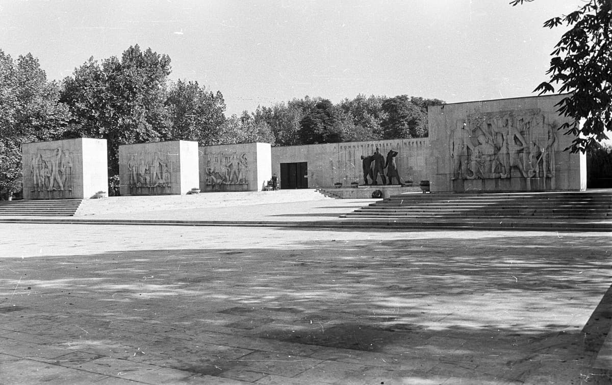 A monumental stone mausoleum with a long wall and trees in a Budapest cemetery