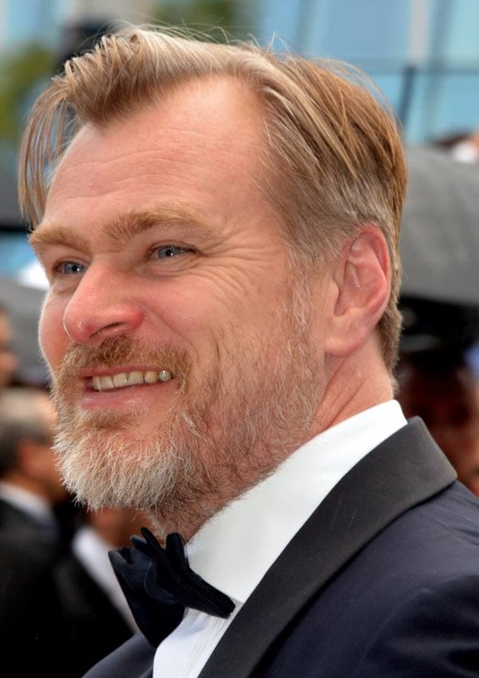 Christopher Nolan in a dark suit, grey hair, at an evening event