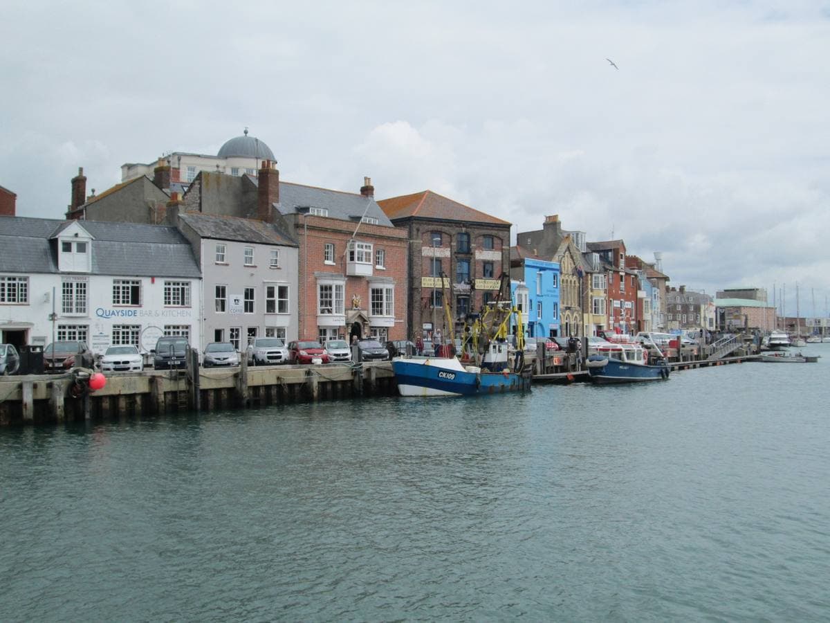 Painted Georgian buildings along a harbour quay with boats moored in front