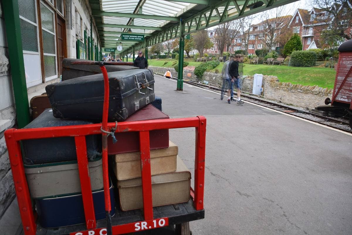 A station platform under a green canopy, old suitcases on a red trolley