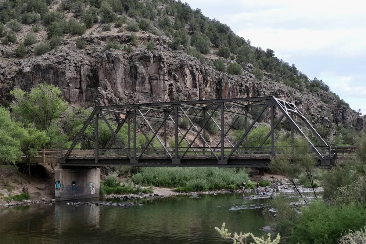 An old steel truss bridge over a green river under dark basalt cliffs