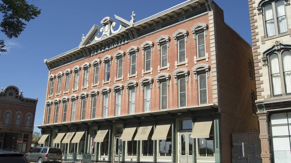 A long three-storey Victorian brick hotel with awnings, cars parked in front