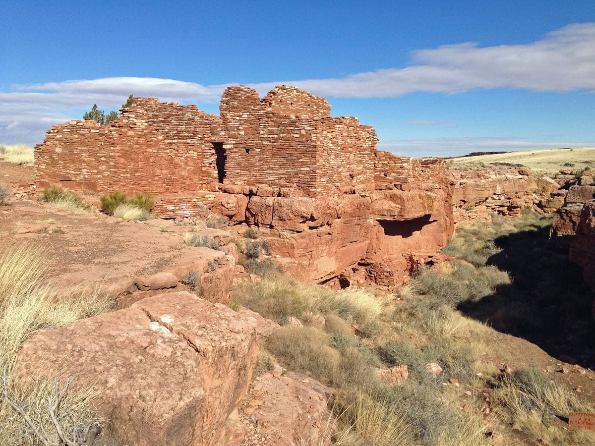 Red sandstone pueblo walls on the rim of a small canyon in grassland