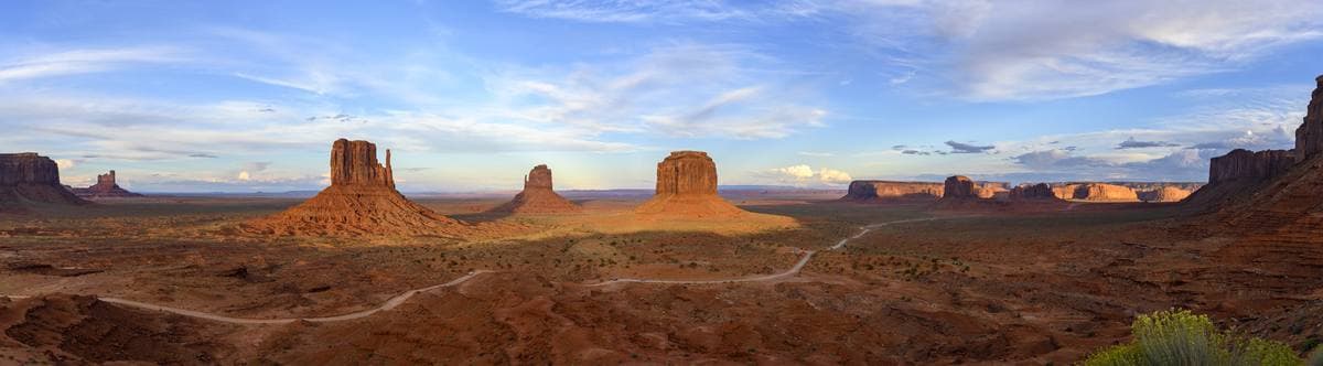 A wide panorama of red buttes across a desert valley under a pale sky