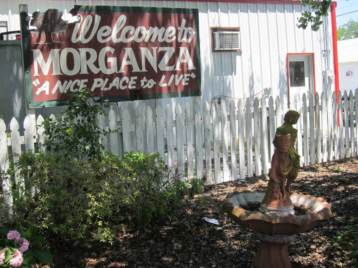 A painted Welcome to Morganza sign on a white building behind a picket fence