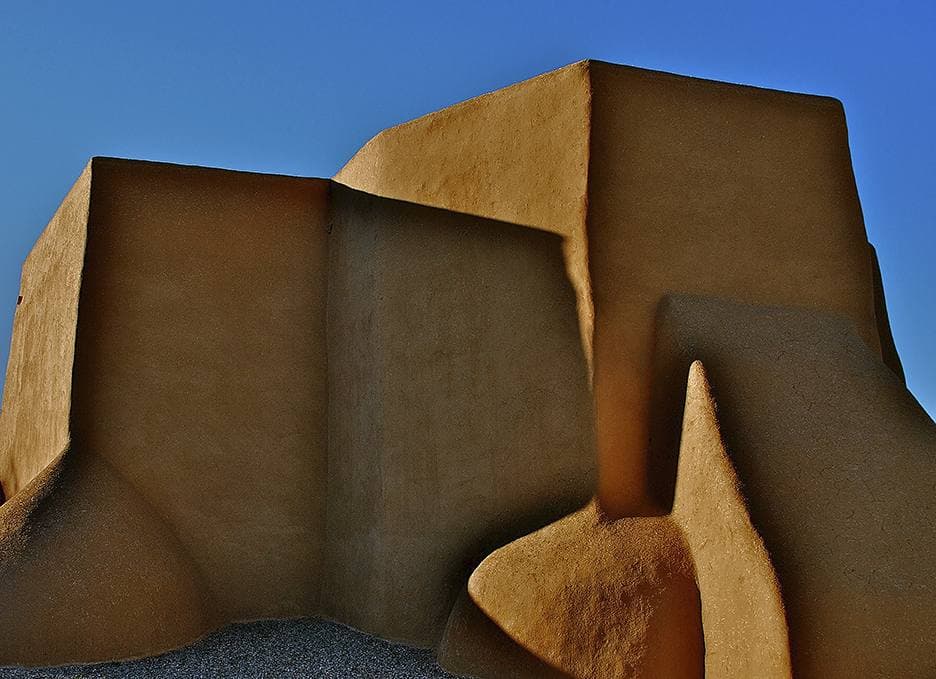 Massive smooth adobe buttresses glowing ochre against a deep blue sky