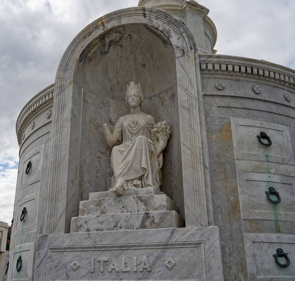 A white marble tomb with a seated statue in a niche above the word ITALIA