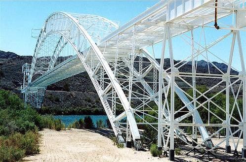 A white steel arch bridge spanning the Colorado River between desert hills