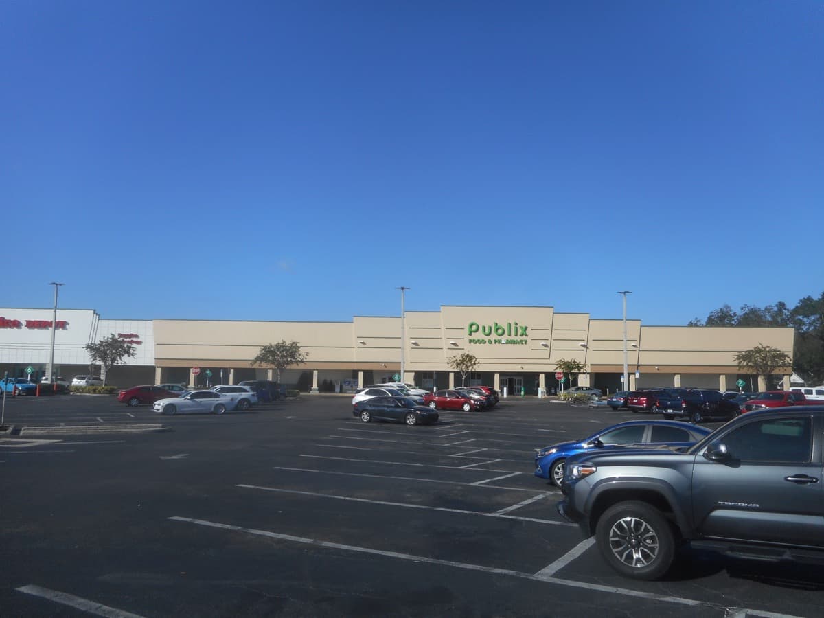 The front of a Publix supermarket in a low shopping centre under a bright sky.