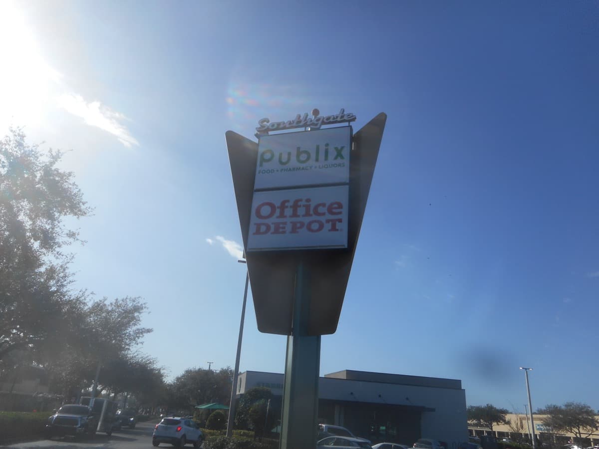 A tall arrow-shaped roadside sign with Southgate in script on top and Publix and Office Depot panels, against a blue sky.
