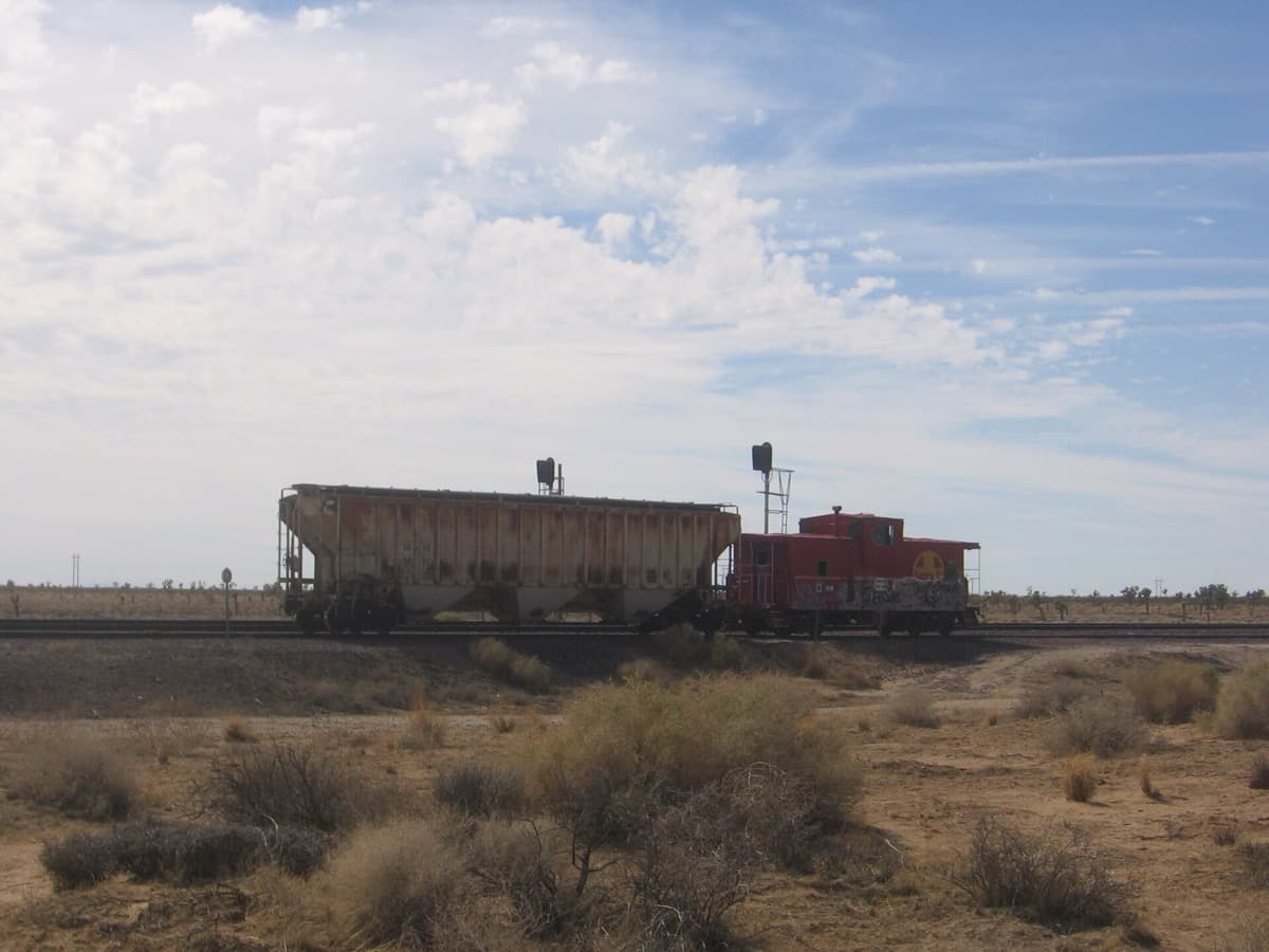 A caboose and a covered hopper car standing on a siding in a desert town
