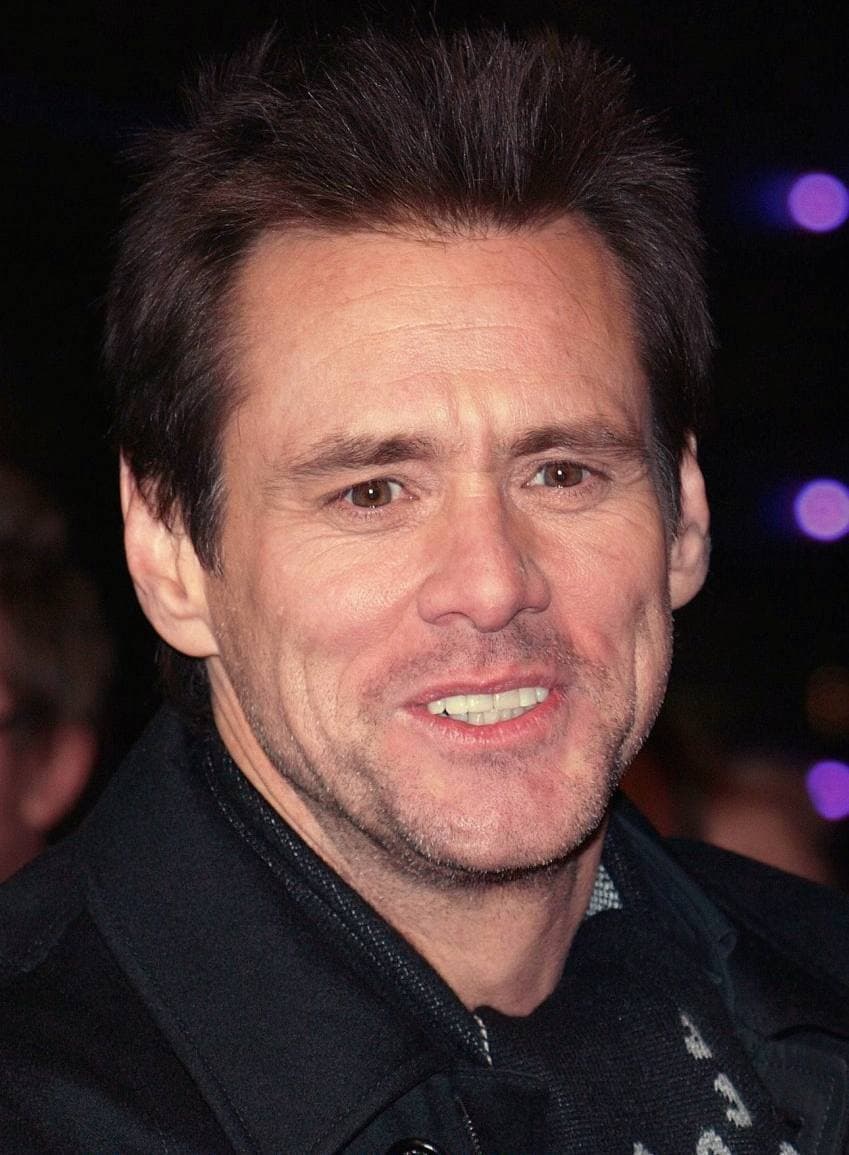 Jim Carrey smiling, in a dark jacket, against a dark background