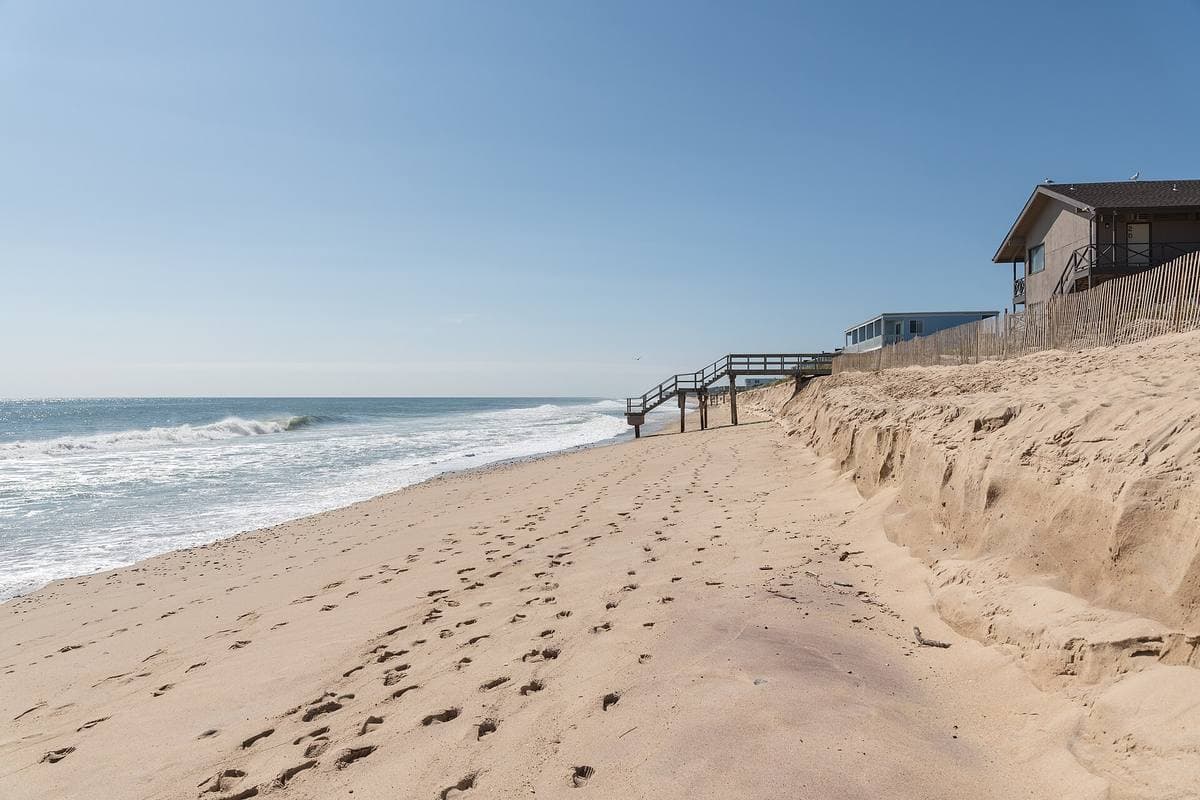 An empty sandy beach with footprints, waves on the left and wooden steps down a dune