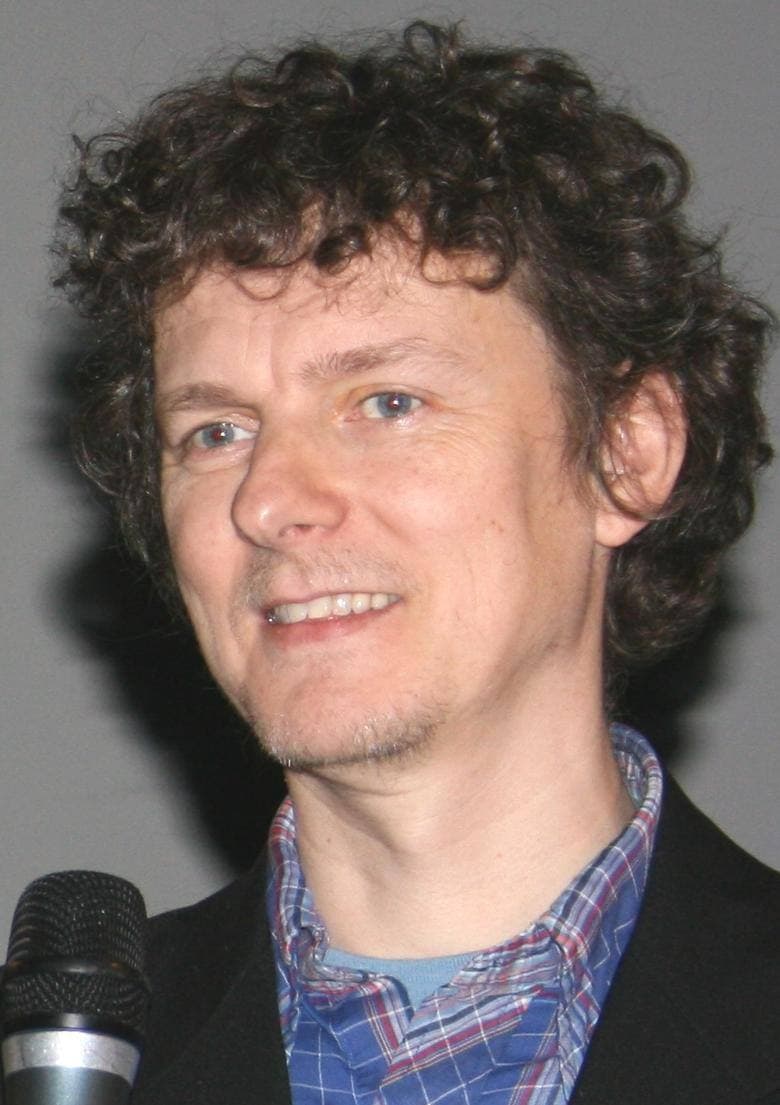 Michel Gondry with curly hair, smiling, holding a microphone