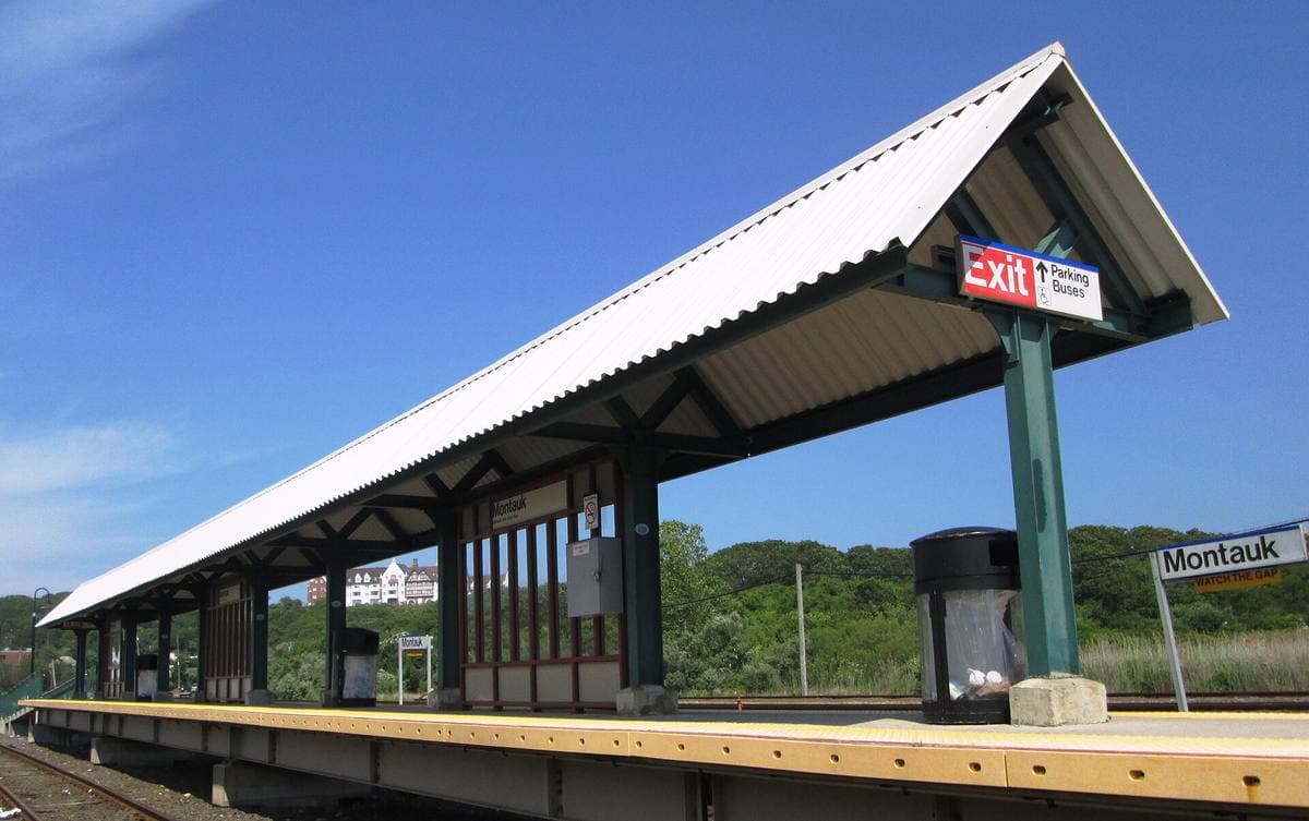 A covered railway platform with a red station sign under a bright blue sky