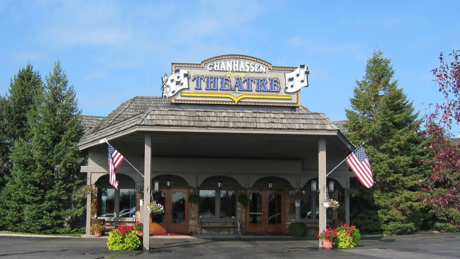 A theatre entrance under a peaked roof with a THEATRE sign, flags and pine trees
