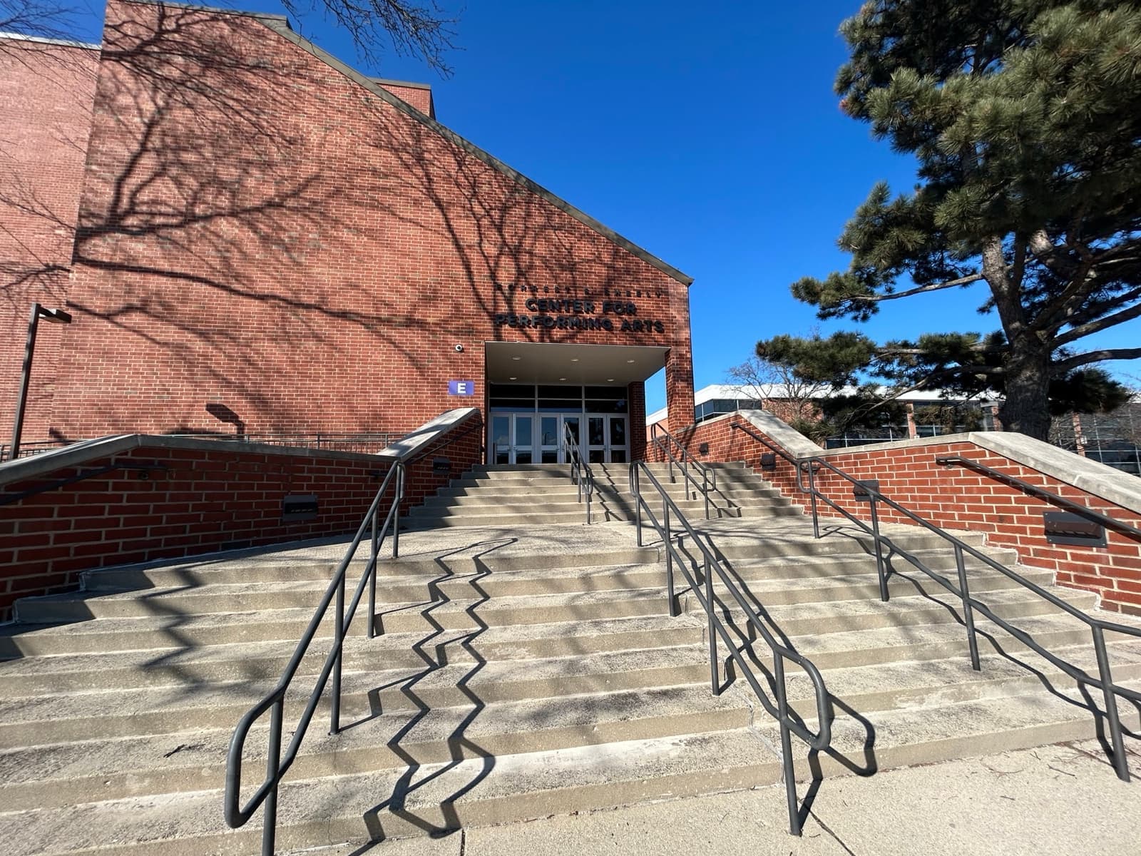 Wide concrete steps with railings up to a brick entrance under a blue sky