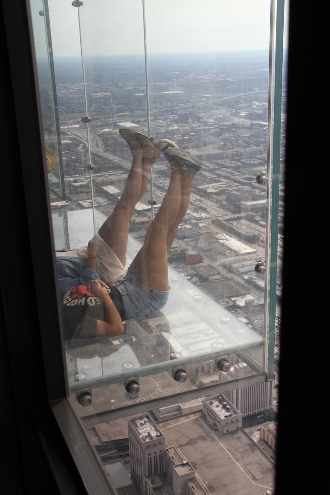 A visitor lying on the glass floor of The Ledge, with streets far below