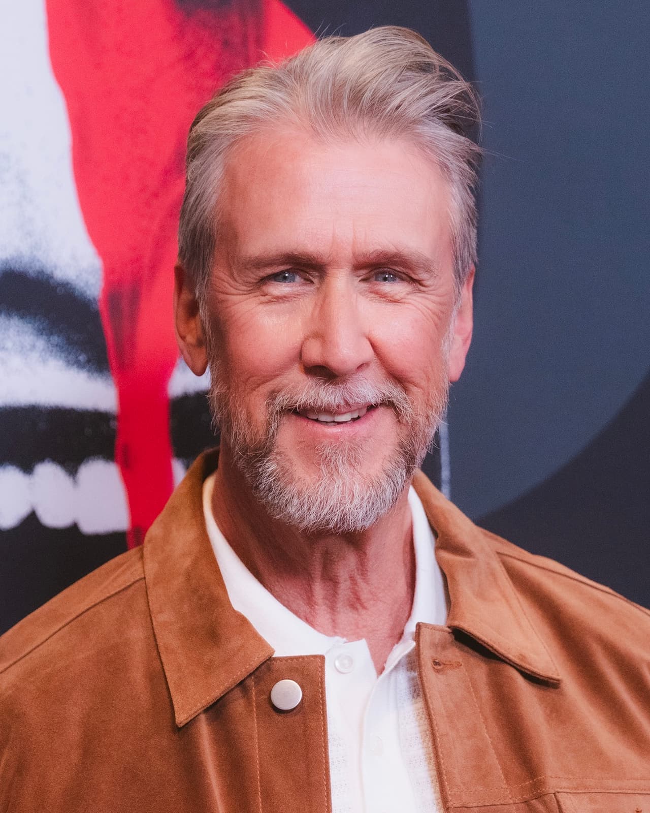 Alan Ruck, grey-haired and bearded, smiling in a tan suede jacket