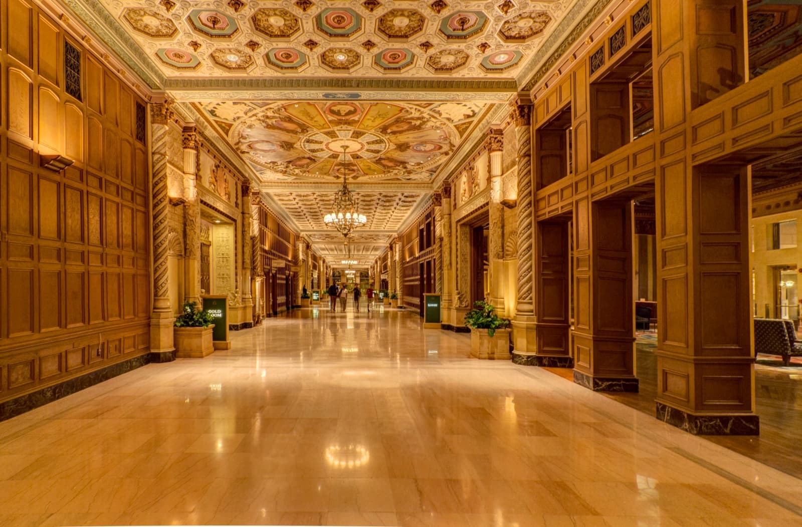 A long gilded hotel corridor with a coffered ceiling and a polished floor