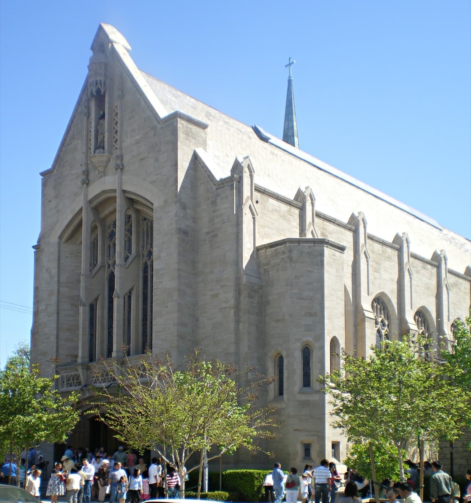 A white Gothic church with a tall spire, people gathered at the door