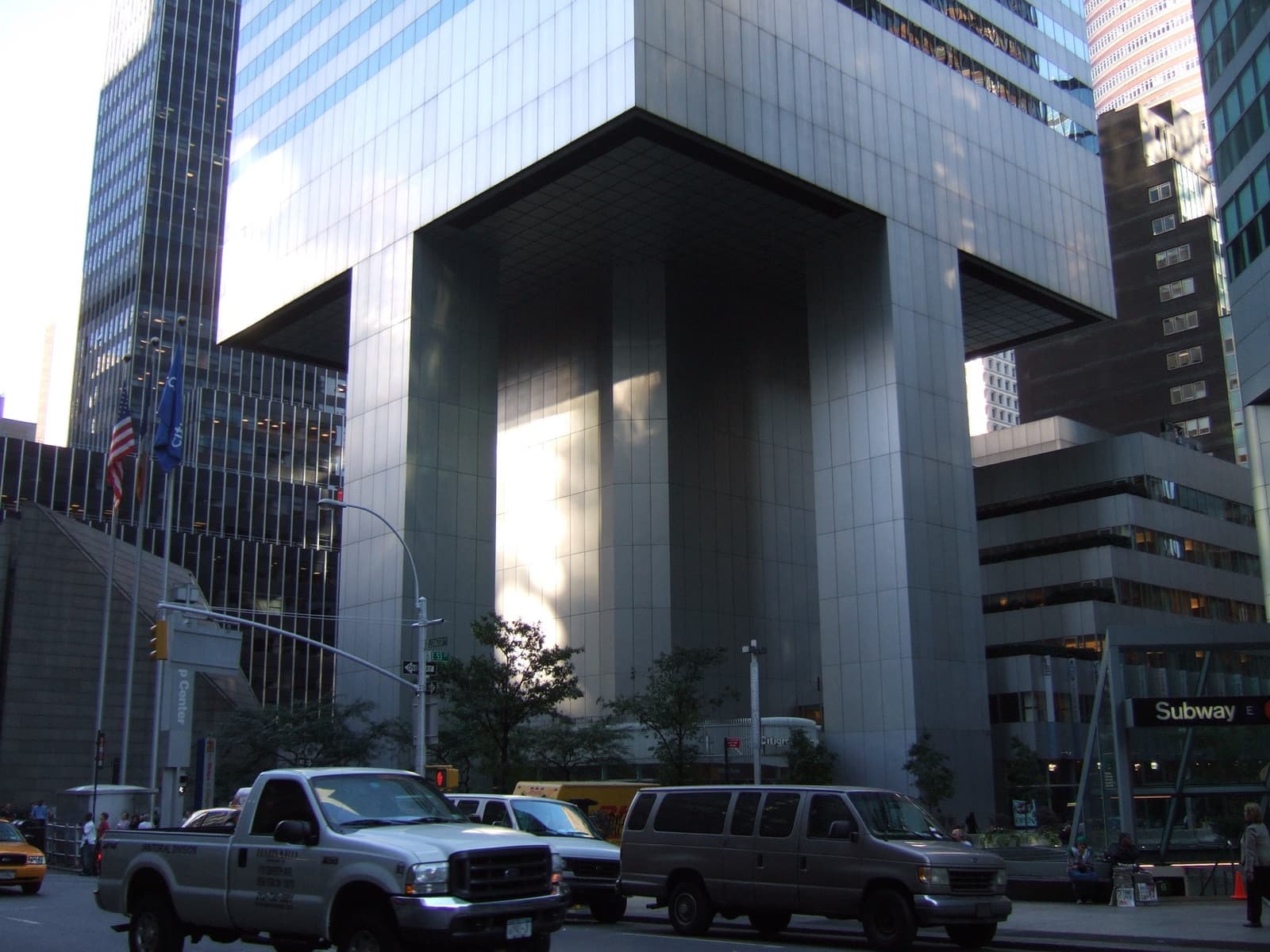 A dark glass tower raised on huge square legs over a plaza, traffic in front
