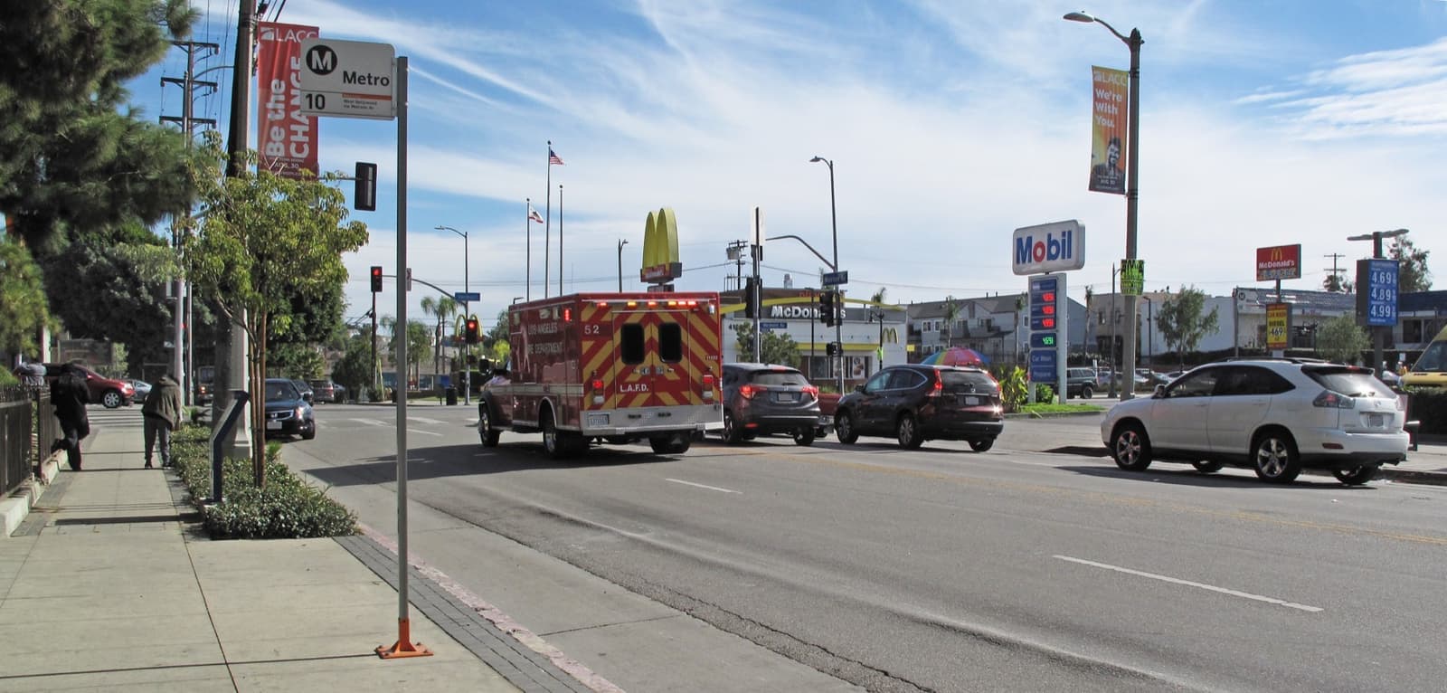 A wide avenue of low shops and traffic under a blue sky