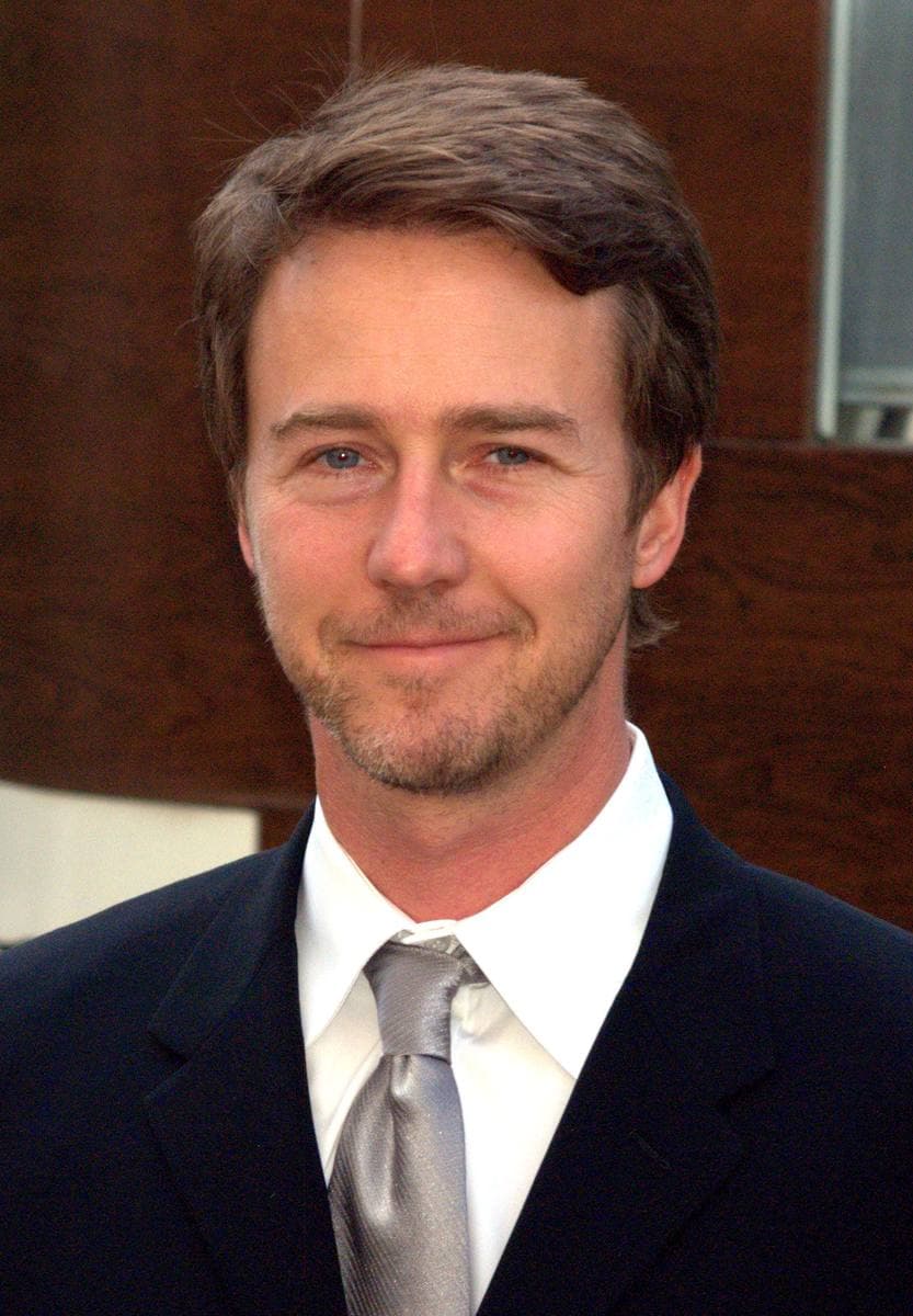 Edward Norton in a dark suit and silver tie, smiling