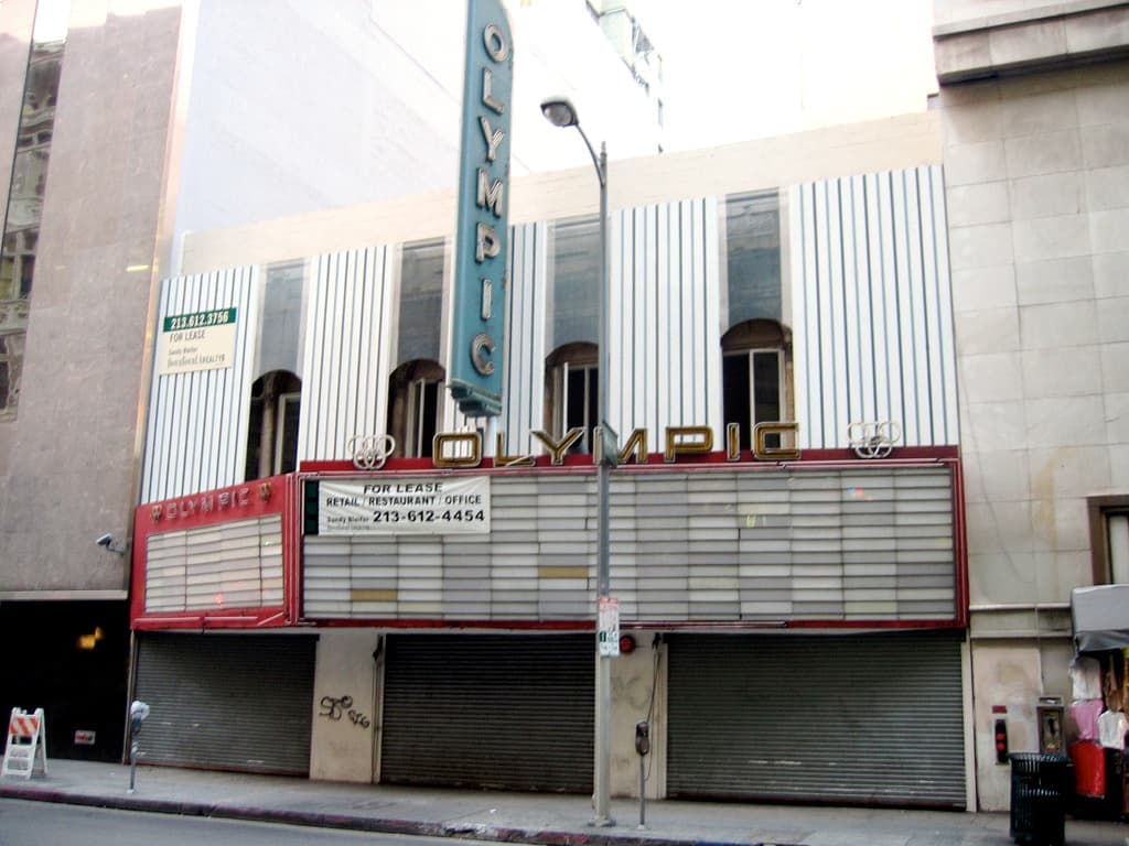 A narrow old cinema front with a vertical Olympic sign and an empty marquee