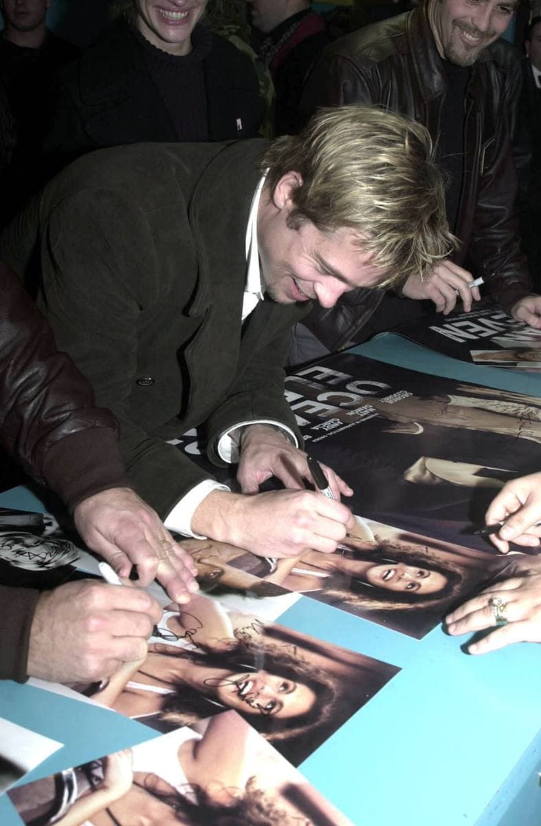 Brad Pitt leans over a table signing photographs for a crowd