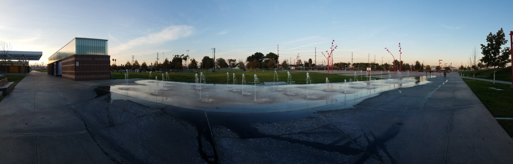 A wide park of lawns and shallow fountains at dusk by the harbour