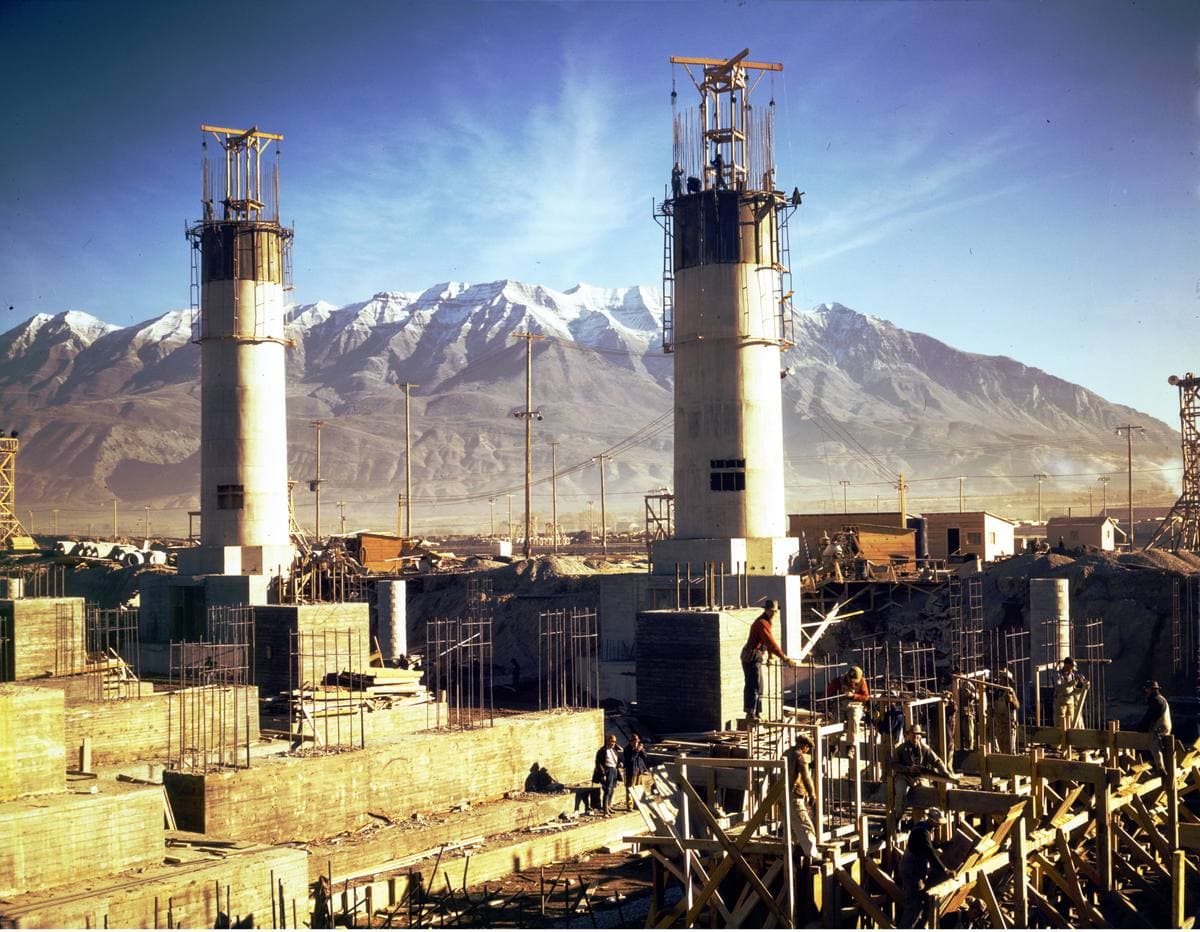 Two tall chimneys over half-built furnaces, snowy mountains behind