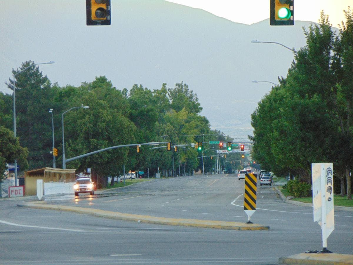 A wide suburban road with traffic lights and trees, mountains behind
