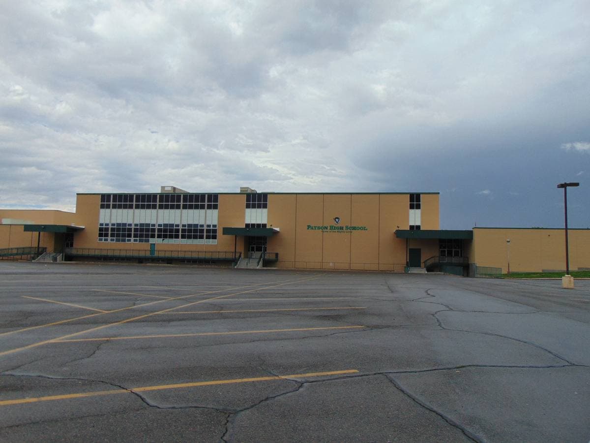 A long low tan school building across an empty parking lot under grey cloud