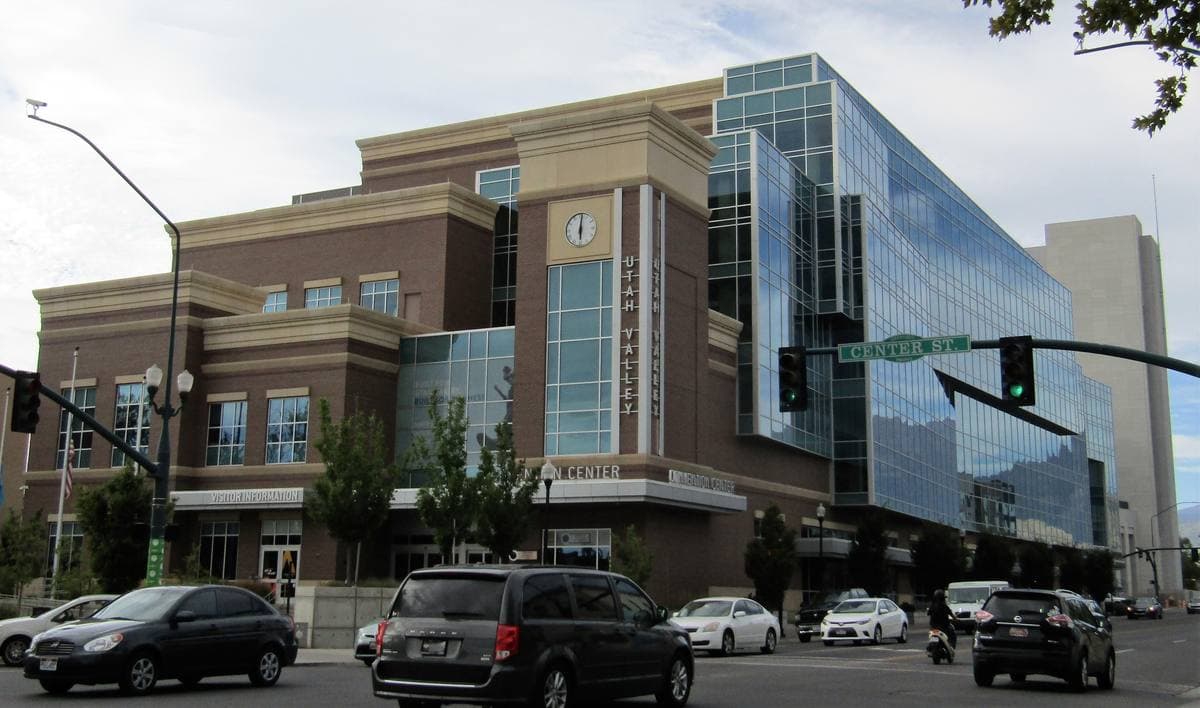 A glass and brick convention centre on a downtown corner with cars at the lights